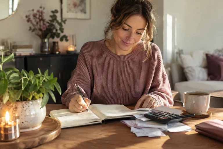 Une femme détendue fait le point sur son budget dans un carnet, à un bureau rangé