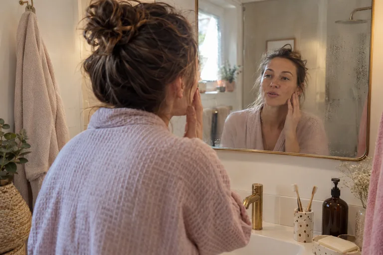 Une femme se regarde dans le miroir de sa salle de bain le matin, l’air naturel
