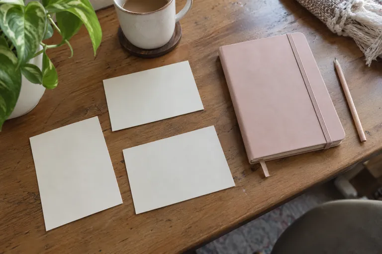 Trois cartes blanches, un carnet rose fermé et un crayon sur une table