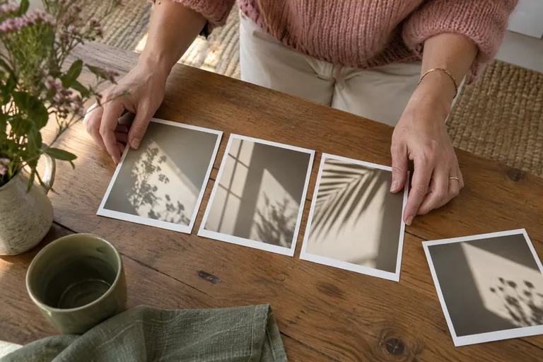 Les mains d’une femme alignent des photographies d’ombres végétales et géométriques sur une table.
