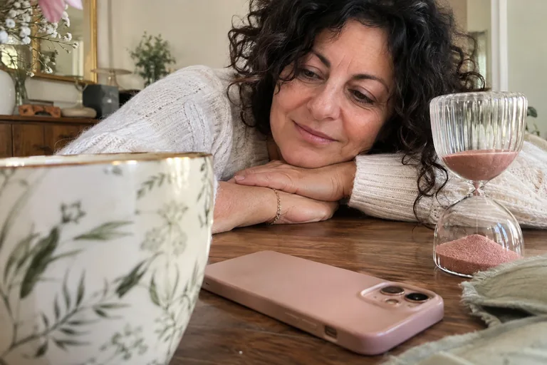 Téléphone face cachée et sablier rose devant une femme accoudée.