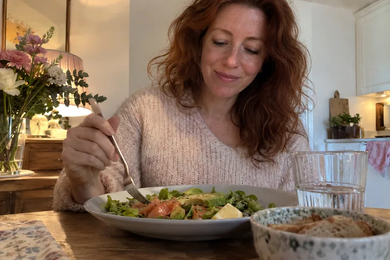 Femme avec une fourchette devant une assiette de salade.