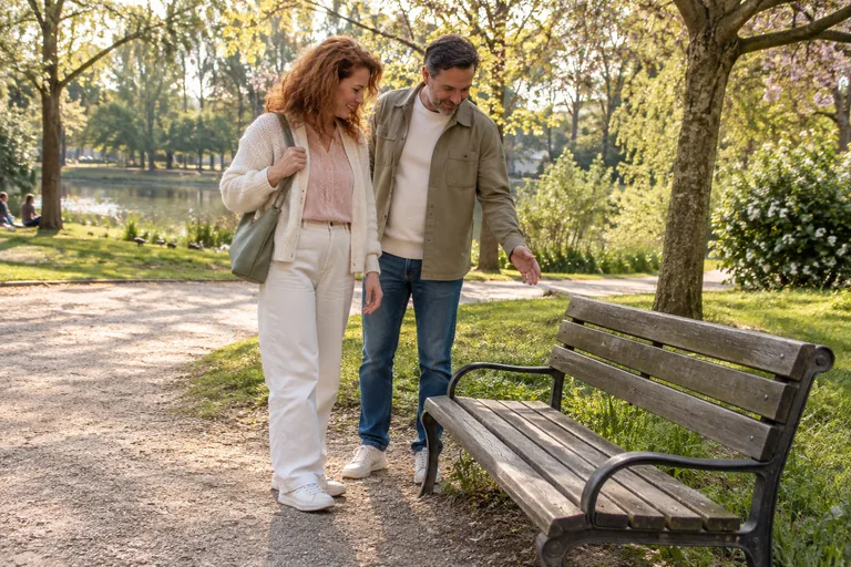 Deux adultes se tiennent près d’un banc dans un parc.