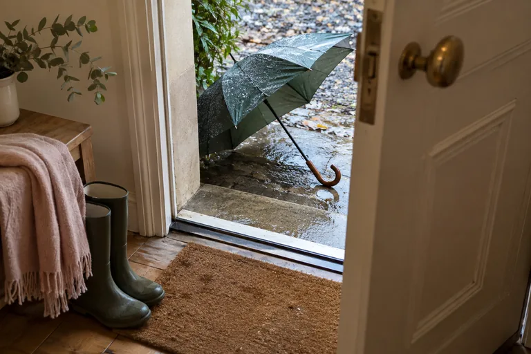 Un parapluie ouvert et mouillé repose dehors derrière une porte entrouverte.