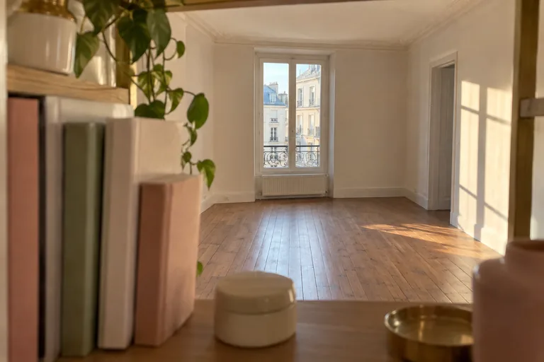 Une pièce vide et sa fenêtre sont vues depuis une étagère garnie de livres fermés.