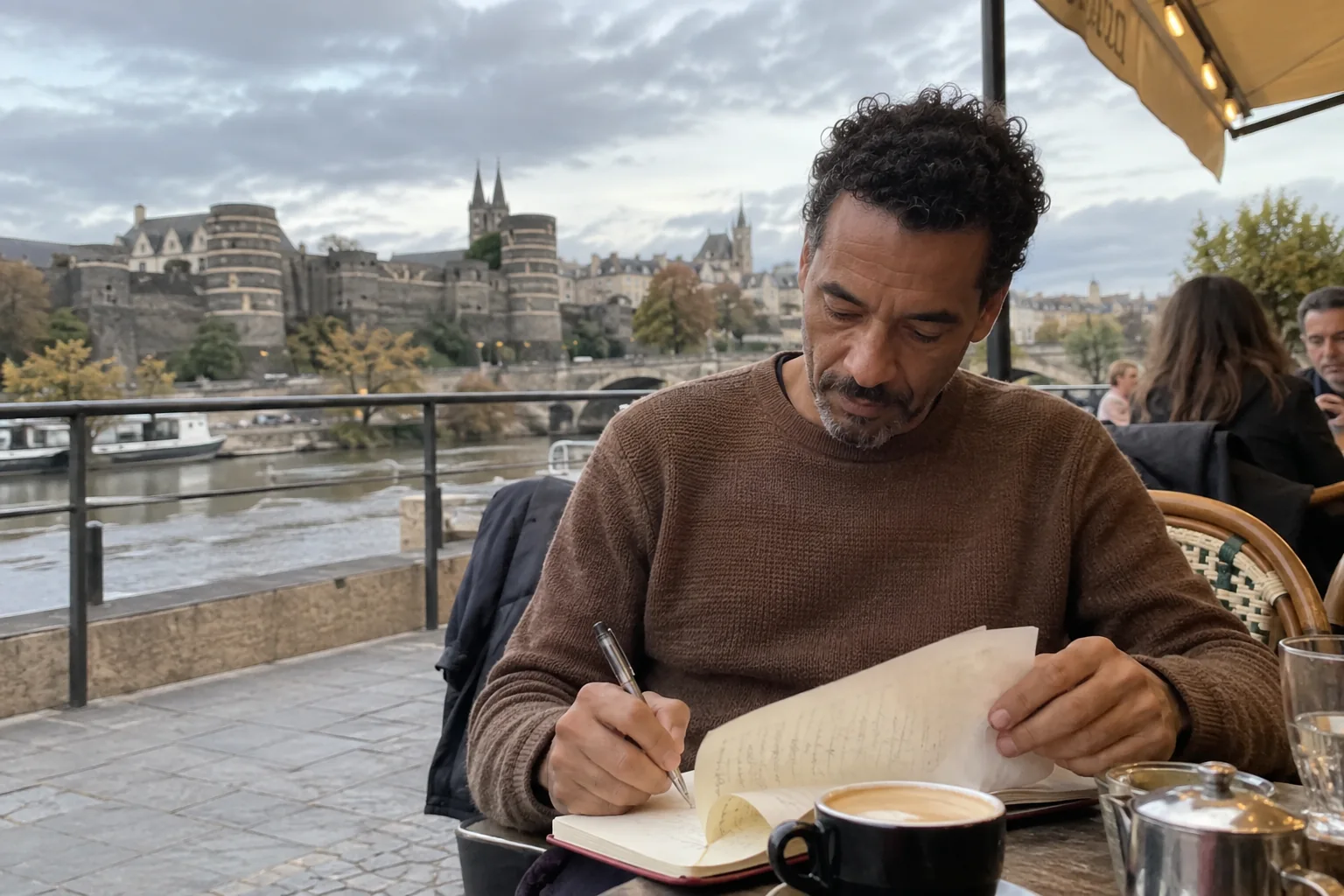 Un homme reprend une page de carnet en terrasse