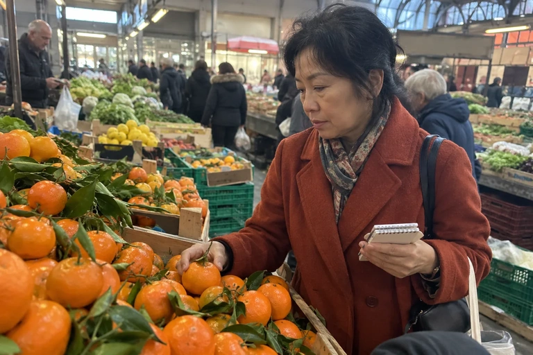 Une femme choisit une mandarine avec un carnet en main au marché