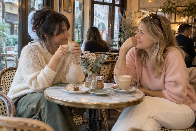 Deux femmes discutant autour de boissons chaudes à une table de café.