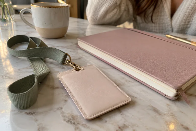 Porte-badge rose retourné avec cordon vert près d’un carnet fermé.