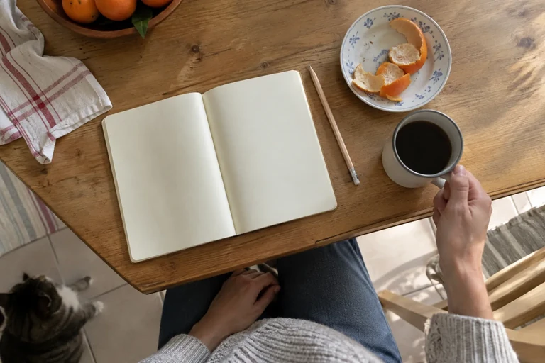Un carnet ouvert, une tasse et des pelures d’orange sur une table.