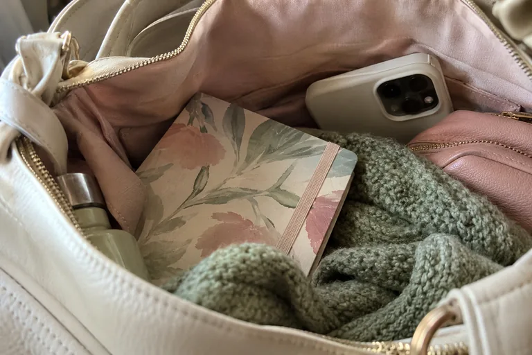 Carnet fleuri fermé et téléphone retourné dans un sac doublé de rose.