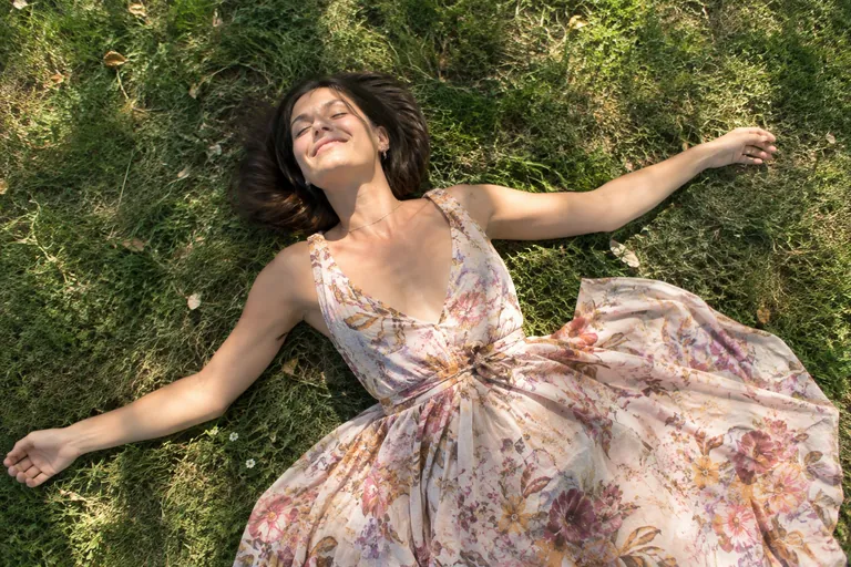 Une femme allongée dans l’herbe, bras ouverts et yeux fermés, savoure le moment