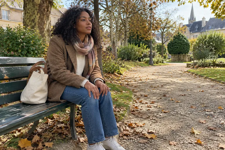 Une femme assise sur un banc dans un parc, un sac à ses côtés