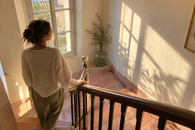Une femme dans un escalier observe les ombres d’une fenêtre sur le mur.