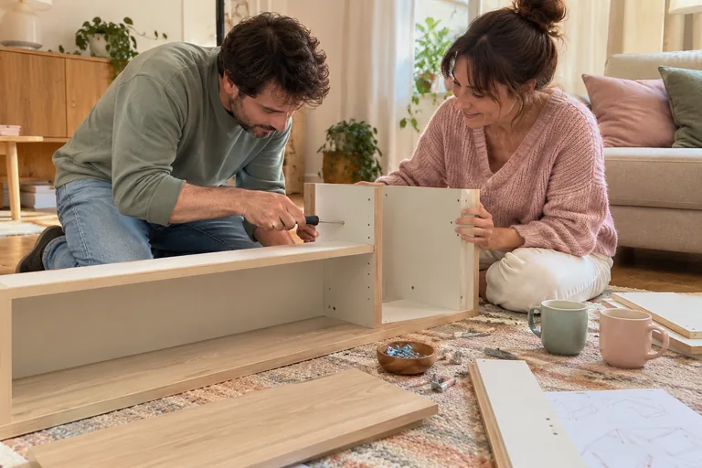 Deux adultes assemblant un meuble près de deux tasses.