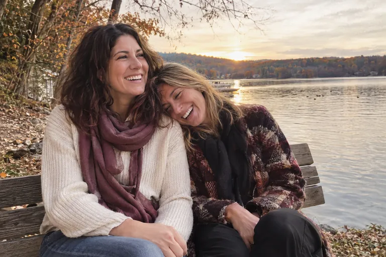Deux amies rient ensemble sur un banc au bord d’un lac en automne