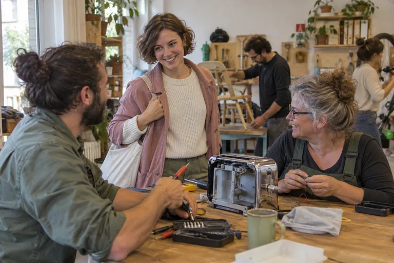 Femme arrivant dans un atelier où des adultes réparent des objets.