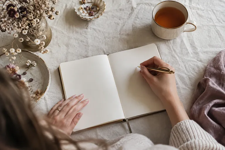 Un carnet ouvert aux pages blanches, un stylo, des fleurs séchées et une tasse de thé