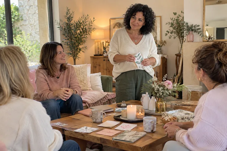 Une femme debout montre une carte illustrée à trois femmes dans un salon.